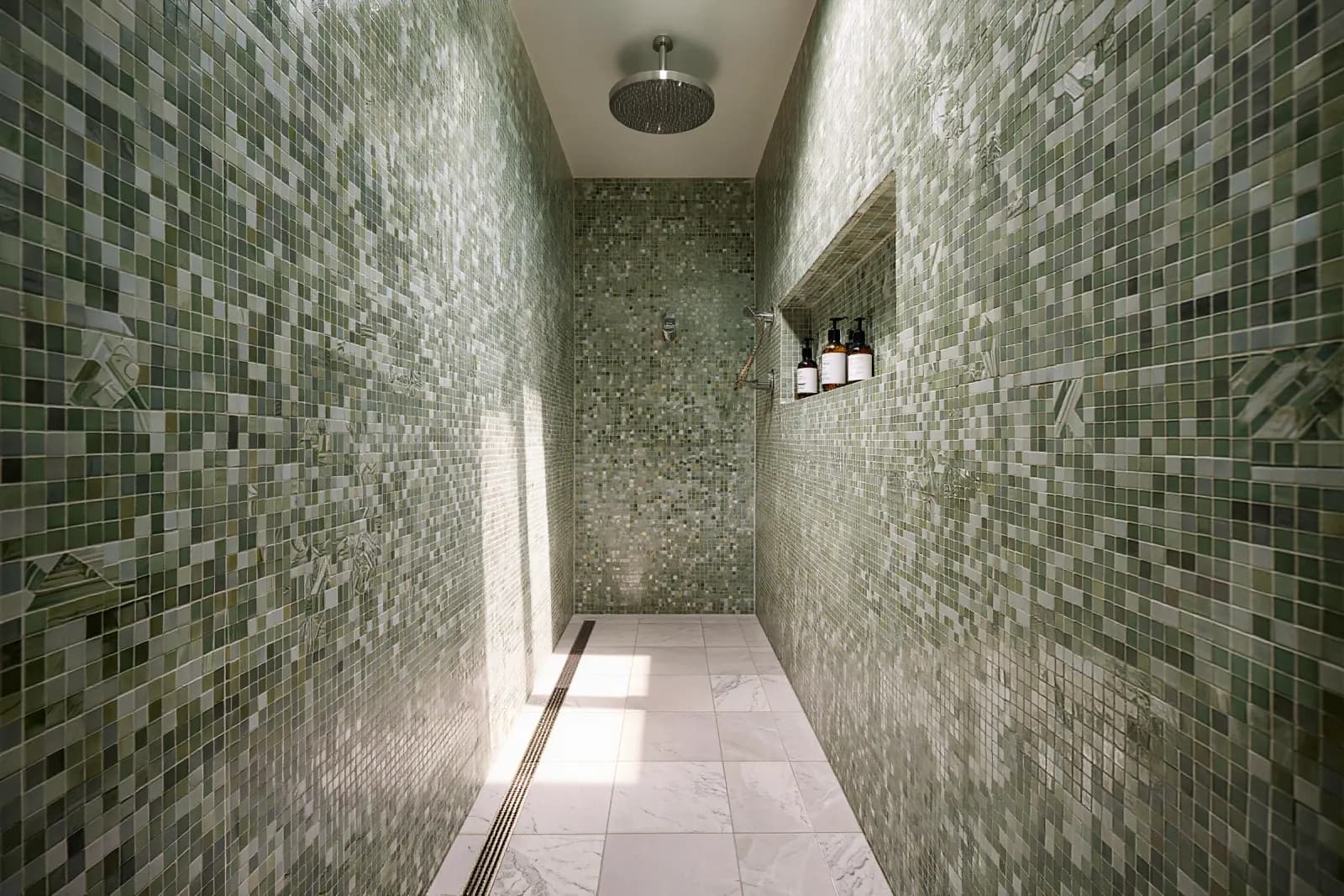 Curbless walk-in shower in sage-green mosaic tile with a linear drain and recessed niche