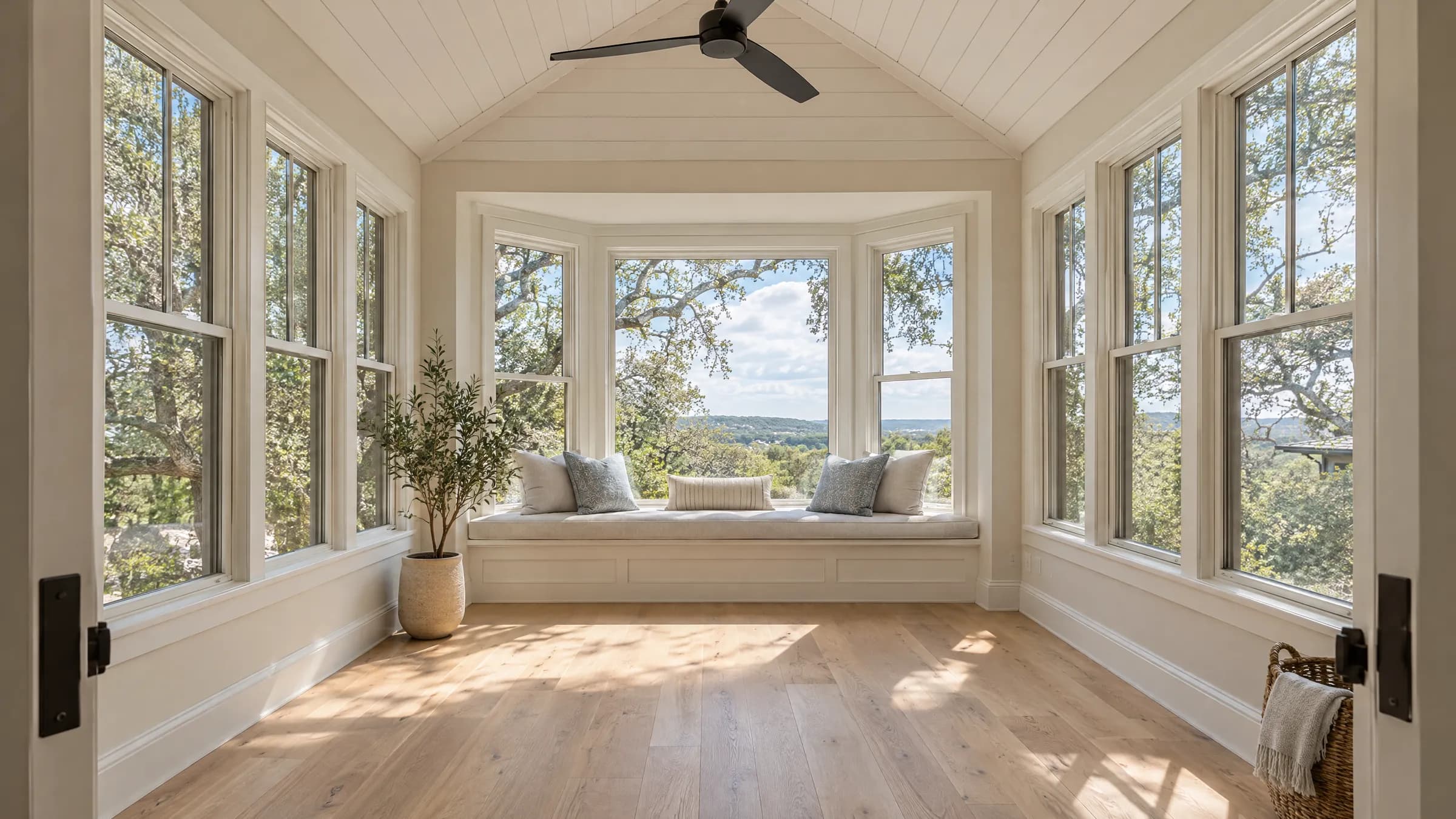 New sunroom addition with a vaulted shiplap ceiling, a bay window seat, and tall windows on three sides looking out at live oaks