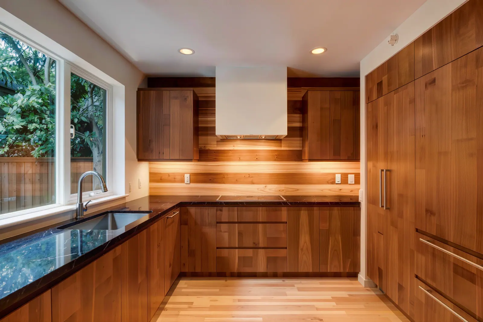 Walnut flat-panel kitchen with black stone counters and a clean boxed plaster hood over the range