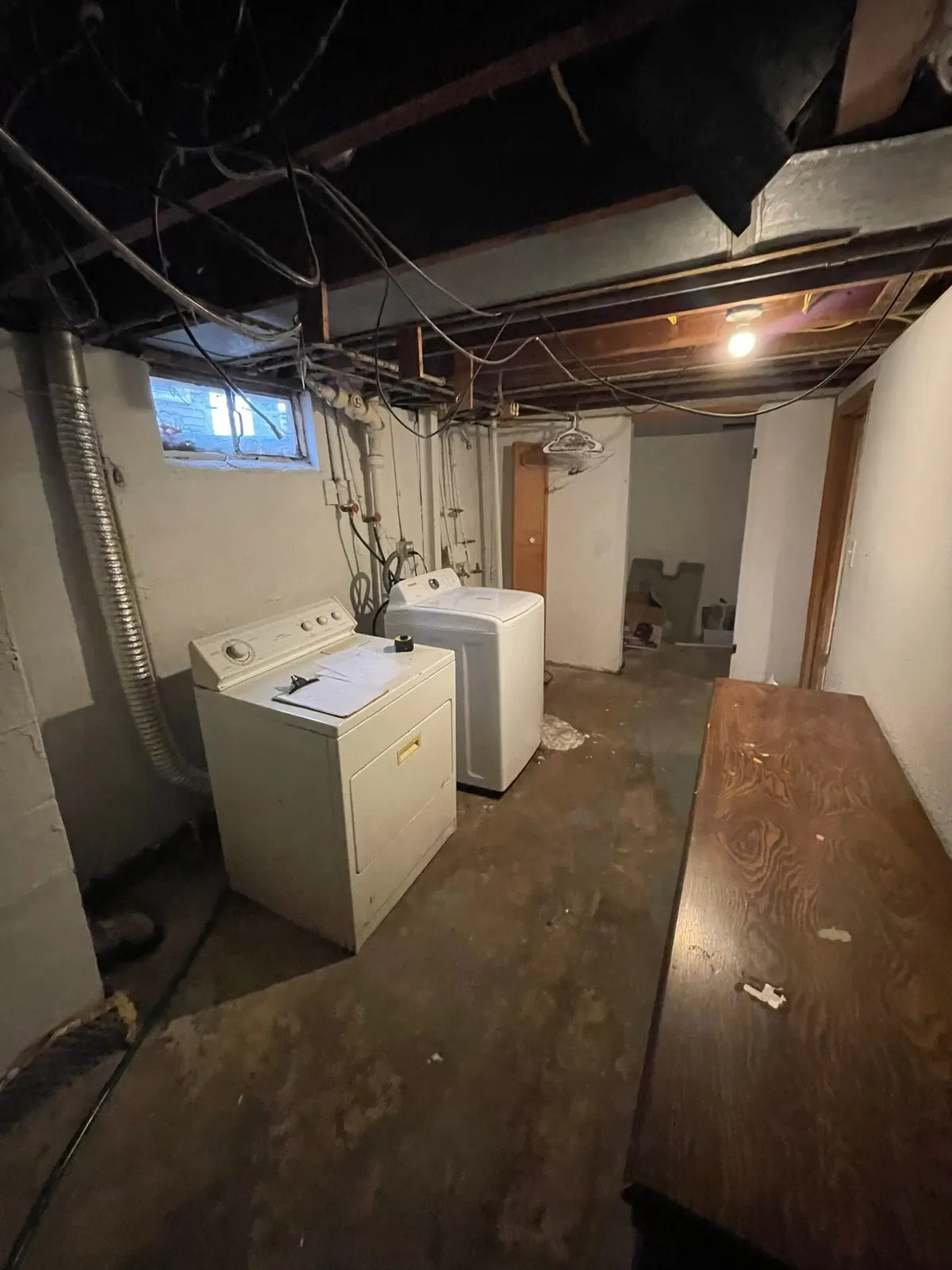Before: the unfinished basement with exposed joists, a bare bulb, and an old washer and dryer on concrete