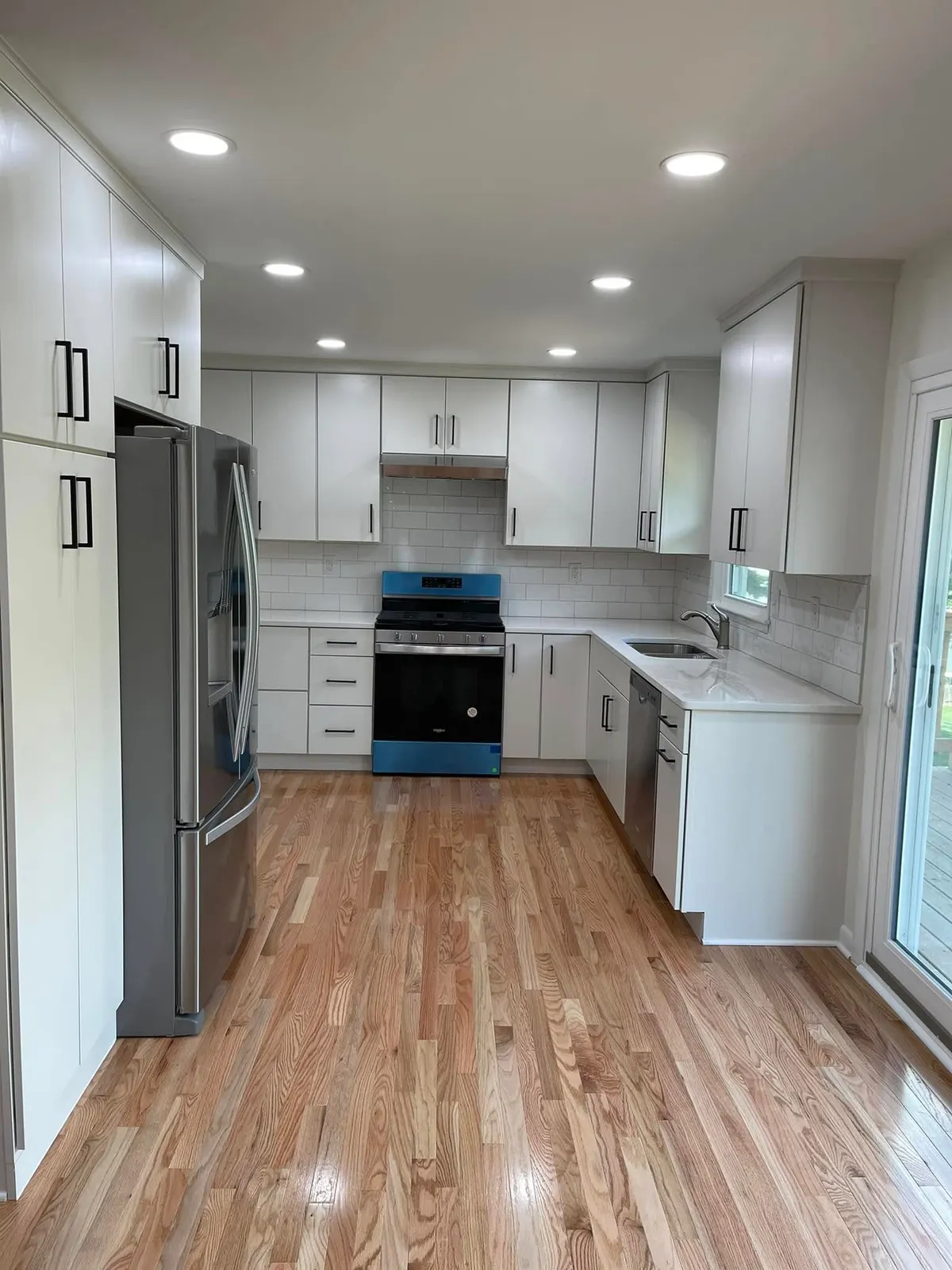 A compact white kitchen with shaker cabinets, subway tile backsplash, stainless range, and new wood-look flooring