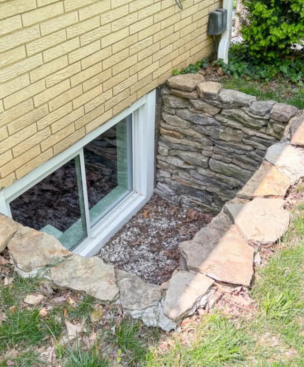 An egress window set into a brick foundation with a stacked-stone well