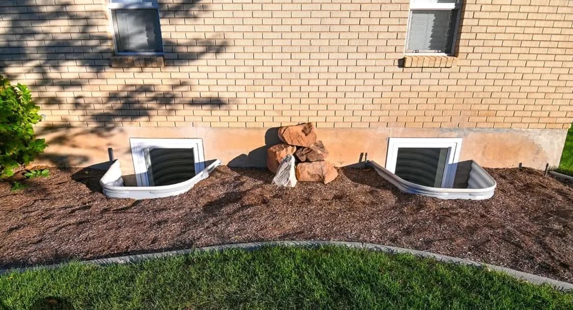 Two new basement windows along a brick foundation with fresh mulch