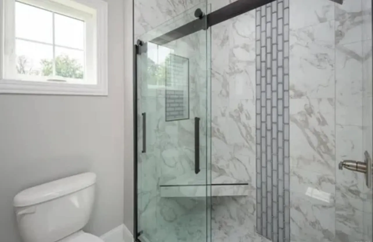 A walk-in shower with marble-look porcelain tile, a vertical mosaic accent strip, and a frameless glass door