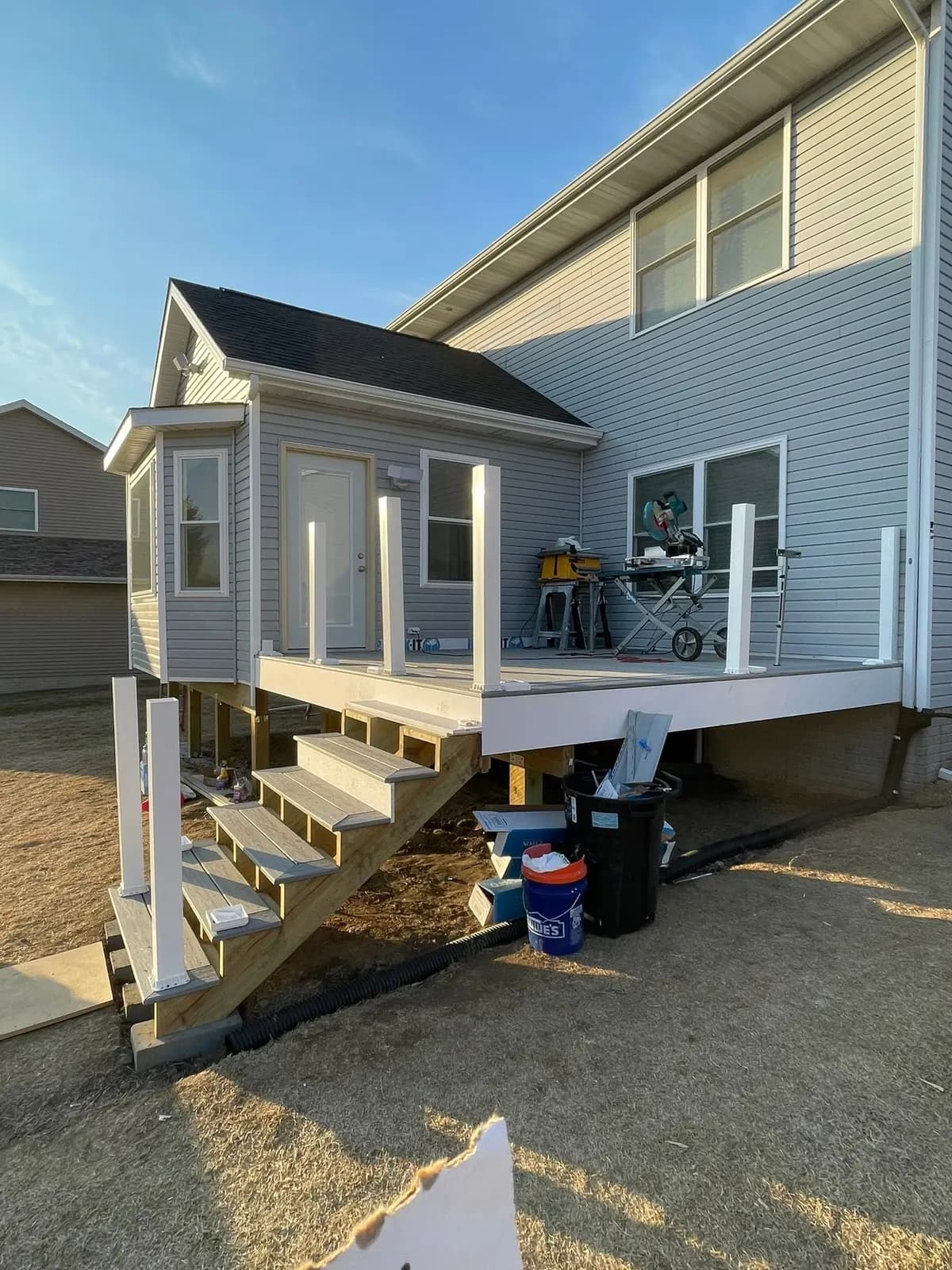 A new deck and stair under construction on the back of a gray two-story house