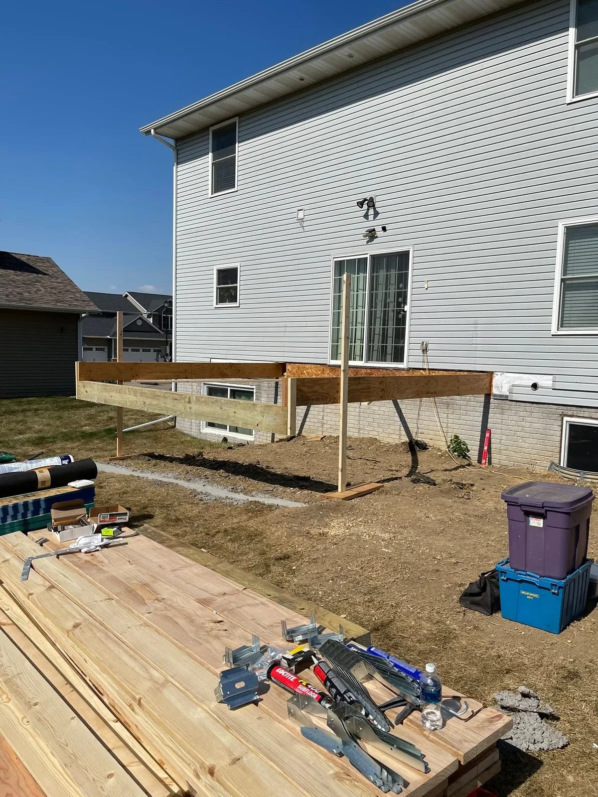 Deck framing in progress with lumber staged on the lot