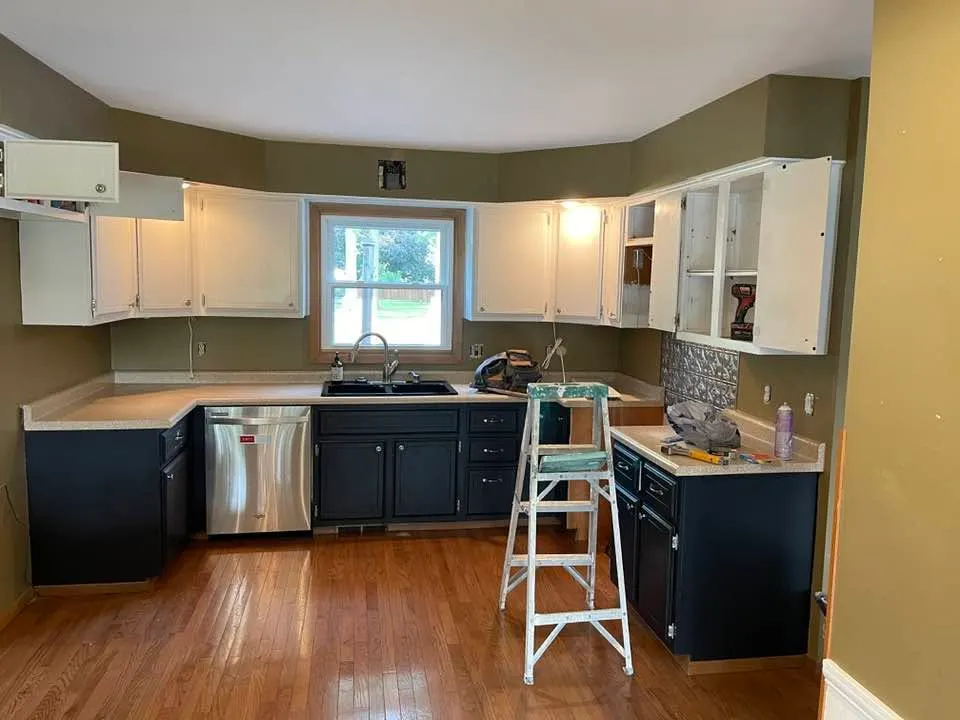 Before: the original kitchen with olive walls, dark lower cabinets, a short peninsula, and a bay window over the sink