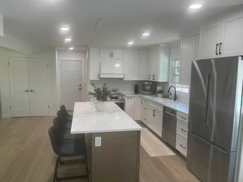 After: the island from the entry, with a stainless refrigerator and light oak floors