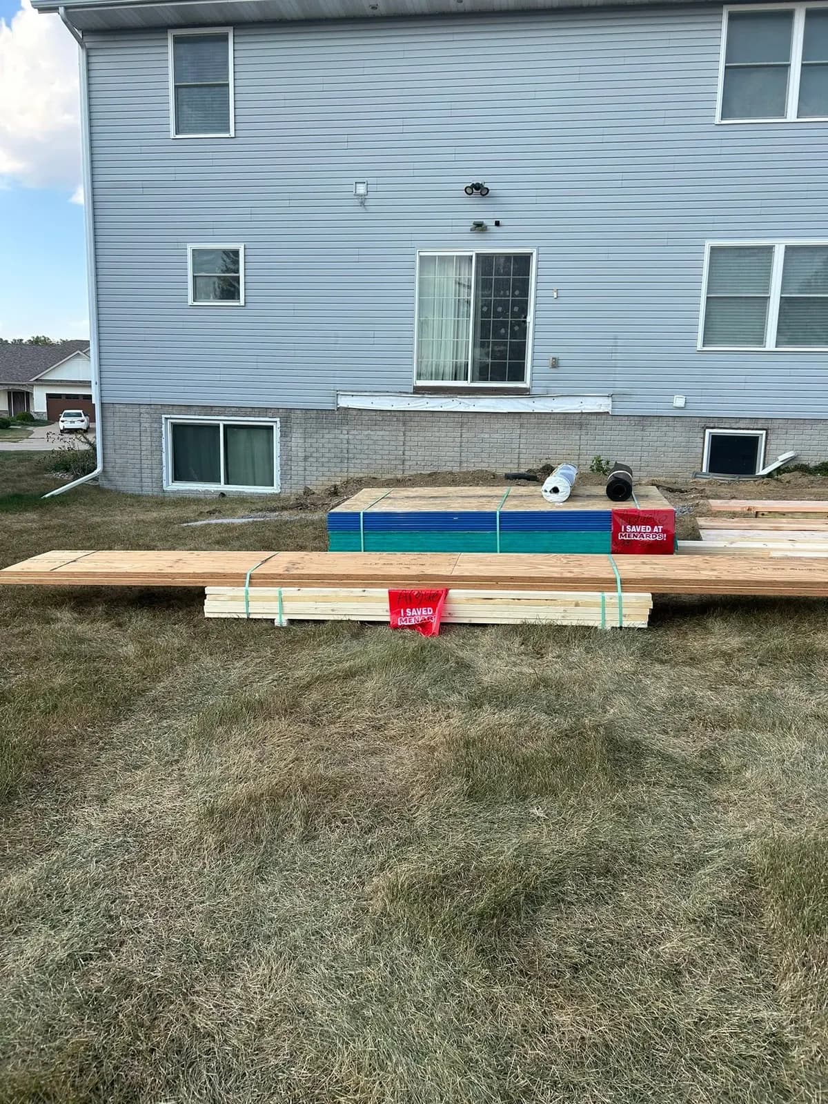 Before: lumber bundles stacked on the back lawn below the blank rear wall of the house