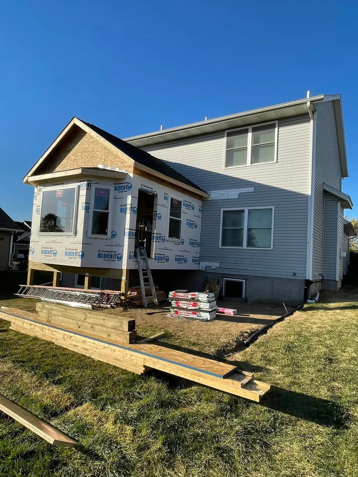 The addition sheathed and house-wrapped, with the roof framed over the bay