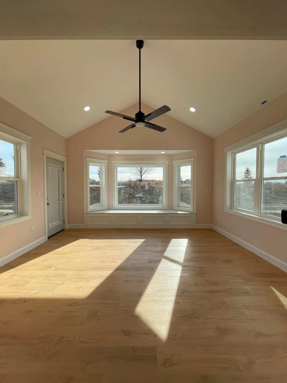 After: the finished sunroom with a vaulted ceiling, ceiling fan, bay window seat, and light oak floors