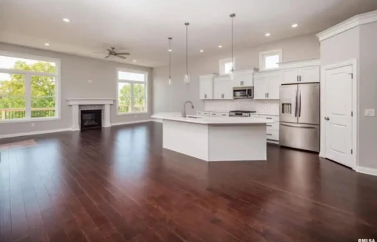 An open great room with dark hardwood floors, a white kitchen island, and a tiled fireplace