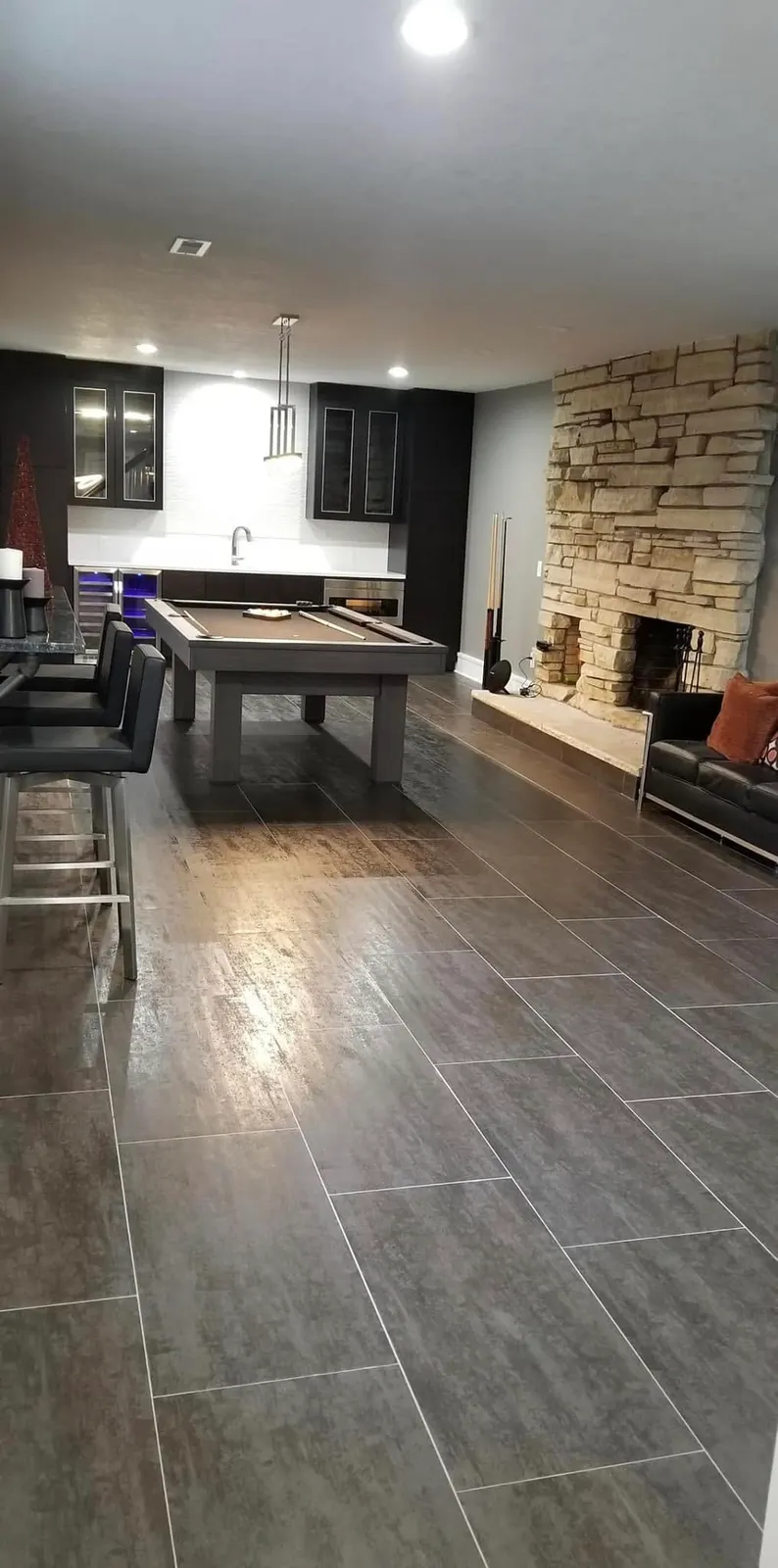 A lower-level game room with a pool table, bar seating, and a stone fireplace